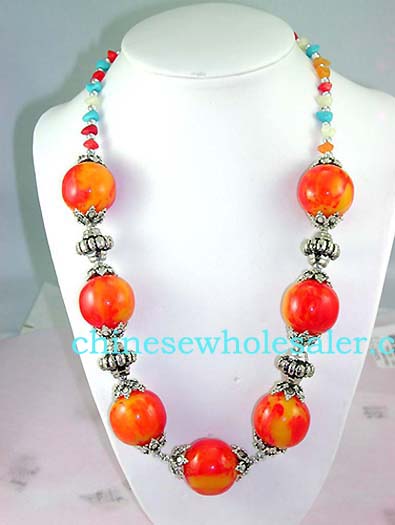 Wholesale fashion online jewelry importer supplying Large orange and red beaded necklace with silver plated chain connecting each bead and changing to small blue, orange, red, and whote beads around neck..    
              
        