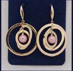 Designer wholesale pearl jewelry store distributing whole fashions. Simulated gold plated hoops circulating around a pink imitation pearl.