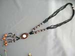 Contemporary balinese art jewelry wholesaler manufactures Multi string black beaded necklace with carved wooden oval emblem and dangling wood beads below 